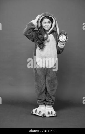 Alarme du matin. Bunny rouge enfant fond. Bébé animal. Temps de comptage. Jour normal de début. Adorable réveil à motif lapin. Petite fille en costume de lapin. Enfant lapin kigurumi. Pyjama fille à motif lapin. Banque D'Images