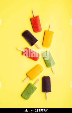 Vue ci-dessus avec glace à la popsicle sur fond jaune. Crème glacée maison avec kiwi, fraises, bleuets et oranges Banque D'Images