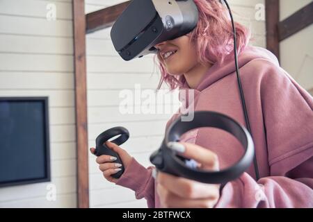 Hipster teen fille port vr casque tenir les contrôleurs jouer le jeu de réalité virtuelle. Banque D'Images