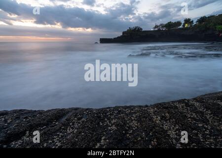 Coucher de soleil spectaculaire et nuageux avec vagues de mer à Pura Penataran Luhur Banque D'Images