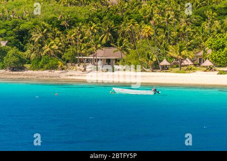 Bungalows sur la plage de sable blanc avec une forêt tropicale en arrière-plan. Eau de la Turuqoise lumineuse avec un bateau au premier plan. Banque D'Images