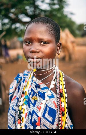 Tribu TOPOSA, SOUDAN DU SUD - 12 MARS 2020: Jeune fille en vêtement ornemental et avec des accessoires colorés regardant l'appareil photo sur un arrière-plan flou de Banque D'Images