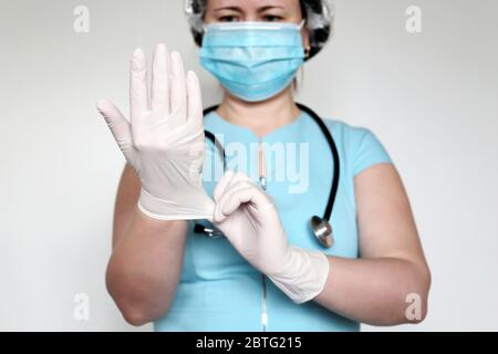 Femme en masque jetable met sur ses gants en latex. Médecin sur examen médical, concept de chirurgie, hygiène, traitement du coronavirus Covid-19 Banque D'Images