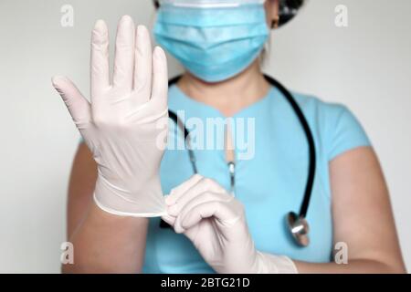 Femme en masque jetable met sur ses gants en latex. Médecin sur examen médical, concept de chirurgie, hygiène, traitement du coronavirus Covid-19 Banque D'Images