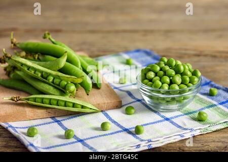 Petits pois frais dans un bol en verre et petits pois dans des gousses sur un chiffon de cuisine. Banque D'Images