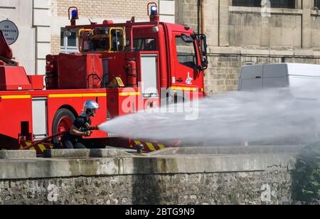Un exercice de formation des pompiers français utilisant un tuyau d'incendie pour pulvériser de l'eau sous haute pression devant un camion-moteur rouge stationné le long du canal de l'Ourcq. Banque D'Images