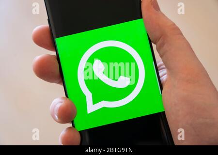 Main d'un homme tenant un smartphone avec un grand logo pour l'application WhatsApp d'appels vidéo et de partage de médias sociaux Banque D'Images