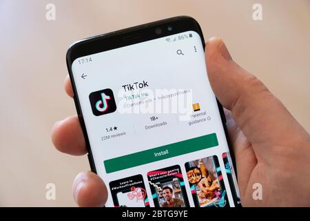 Main d'un homme tenant un smartphone affichant l'écran d'installation de Google Play pour l'application de partage de vidéos sur les réseaux sociaux Tik Tok Banque D'Images