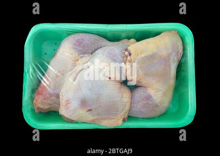 Pattes de poulet crues en vert, emballées sur fond noir isolé Banque D'Images