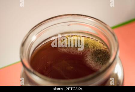 On peut voir un demi-pot sans couvercle avec compote de framboise, qui est complètement recouvert de fils de moisissure jaune et grise. Photo sur bac blanc-rose Banque D'Images