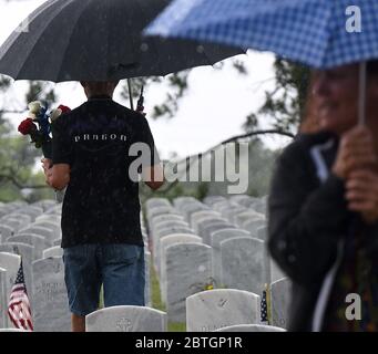 Un homme tenant un parapluie transporte des fleurs jusqu'à une tombe sous la pluie le jour du souvenir au cimetière national du Cap Canaveral. Banque D'Images