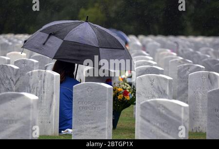 Une femme tenant un parapluie est assise près d'une tombe sous la pluie avec un bouquet de fleurs le jour du souvenir au cimetière national de Cape Canaveral. Banque D'Images