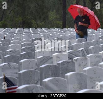 Un homme tenant un parapluie paie ses respects par une pierre d'angle sous la pluie le jour du souvenir au cimetière national de Cape Canaveral. Banque D'Images