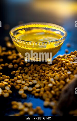 Pâte de pois chiches fraîchement bouillie dans un bol en verre sur une surface noire avec quelques lentilles de pois chiches crues. Banque D'Images