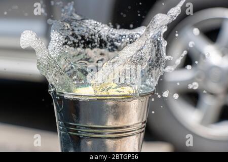 Une éponge tombe dans le seau avec une éclaboussure de détergent. Laver à la main la voiture à l'eau savonneuse. Banque D'Images