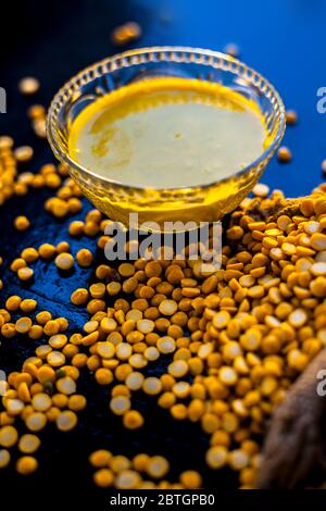 Pâte de pois chiches fraîchement bouillie dans un bol en verre sur la surface noire avec quelques lentilles de pois chiches crues. Banque D'Images