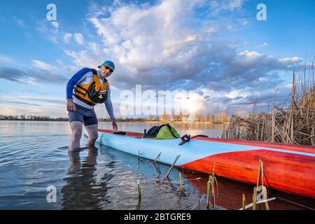 paddler homme senior avec son stand en paddleboard sur un lac calme, paddling solo comme forme physique et entraînement avec distancement social Banque D'Images