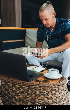 Un indépendant, un jeune homme d'affaires, qui travaille à distance tout en étant assis dans un café avec une tasse de café le matin. Utilise la technologie moderne. Un lapto Banque D'Images