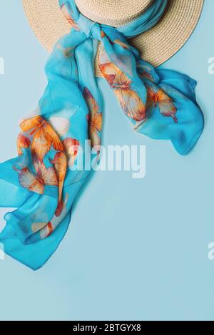 Chapeau de paille avec foulard sur fond bleu. Étapage à plat, vue du dessus avec espace pour copier. Banque D'Images