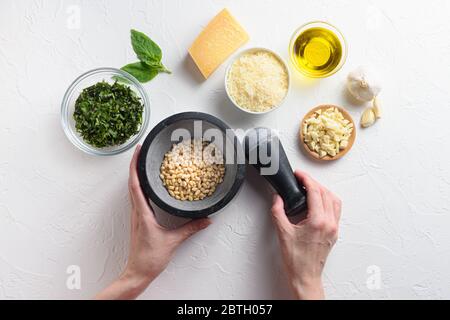 Pesto sauce cuisson avec les mains et le mortier de la femme . Basilic, huile d'olive, parmesan, ail, pignons. Vue de dessus avec espace tableau blanc pour votre texte Banque D'Images