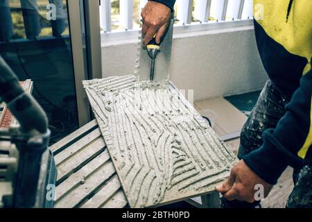 Un constructeur professionnel smear la colle de ciment sur le carreau de céramique avec une truelle. Rénovation concept réparation, révision, mise à plat sous contrat. Banque D'Images