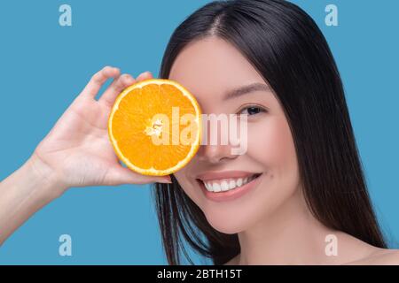 Jeune femme souriante, portant une tranche d'orange et se sentant heureuse Banque D'Images