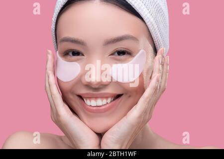 Une jeune fille asiatique souriante dans un foulard blanc qui applique des taches sous les yeux Banque D'Images