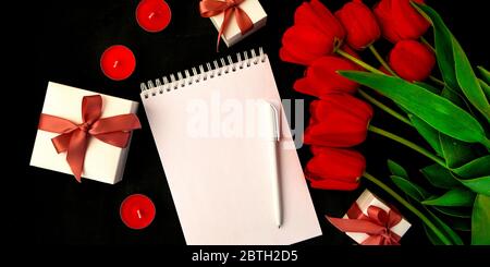 Tulipes rouges, carte vierge ou bloc-notes avec stylo et bougies, boîte cadeau isolée sur fond noir, espace de copie pour le texte Banque D'Images