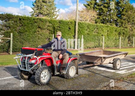 Annat, Canterbury, Nouvelle-Zélande, mai 26 2020 : un agriculteur à la retraite lance une remorque derrière son quad pour recueillir des haies sur une route rurale Banque D'Images