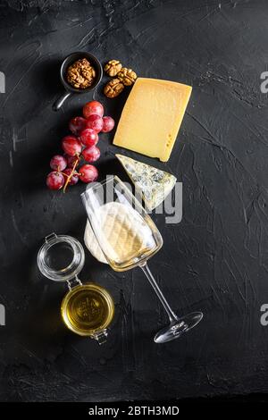 Sélection de hors-d'œuvre au fromage ou d'en-cas à la baleine. Variété de fromages français, raisins, noix de pécan, vin sauvignon blanc et miel sur fond noir, Banque D'Images
