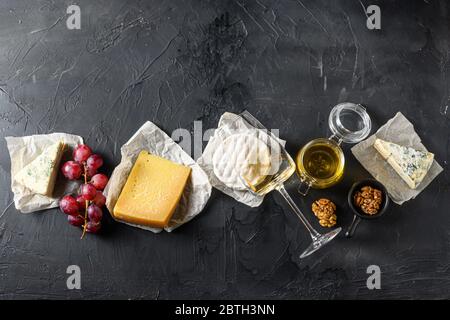 Sélection de hors-d'œuvre au fromage ou d'en-cas à la baleine. Variété de fromages français, raisins, noix de pécan, vin sauvignon blanc et miel sur fond noir, Banque D'Images