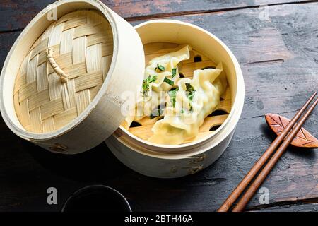 Gyozas potstickers boulettes chinoises dans un cuiseur vapeur en bois avec sauce soja herbes fraîches et baguettes sur la table en bois ancienne vue de près. Banque D'Images