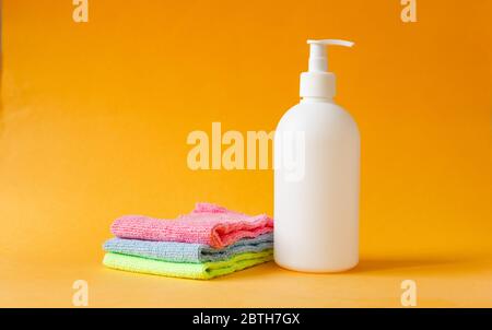 Trois serviettes de nettoyage colorées et une bouteille blanche pour nettoyer les sols sur fond jaune. Banque D'Images