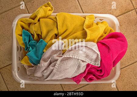 Vue de dessus des serviettes multicolores dans un panier à linge en plastique sur le sol carrelé. Banque D'Images