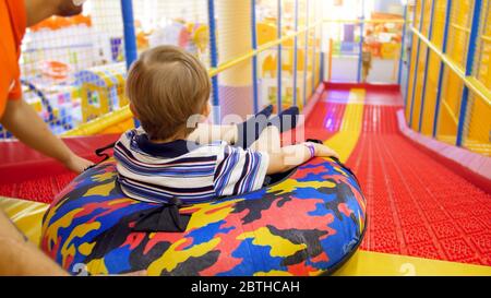 Un petit garçon mignon qui descend sur la glissade sur l'anneau gonflable en forme de beignet dans la salle de jeux pour enfants du centre commercial Banque D'Images