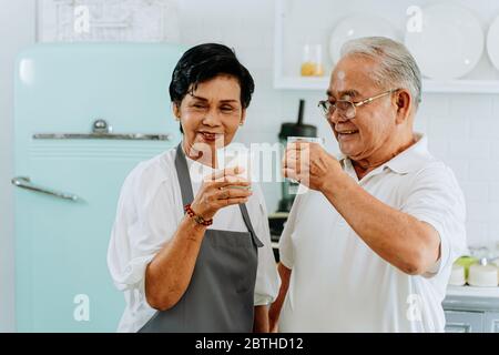 Un couple asiatique senior heureux qui boit du lait chez lui. 70 ans, un homme et une femme mariés tenant un verre de lait dans la cuisine. Banque D'Images
