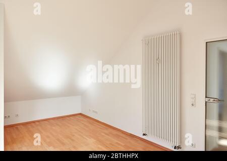 Chambre lumineuse vide avec plafond en pente dans appartement mansardé avec radiateur Banque D'Images