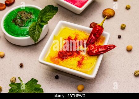 Hummus, nourriture végétalienne (végétarienne) saine. Trois types variés : classique, menthe et betterave. Haricots secs édamame, morceaux de pain pita, épices. Béton de pierre Banque D'Images