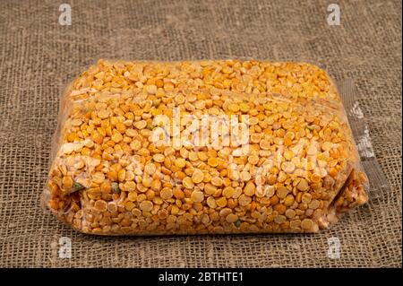 Petits pois jaunes dans un sac de cellophane sur fond de toile de jute à texture grossière. Grains traditionnels pour la préparation de soupes et de porridges. Gros plan Banque D'Images