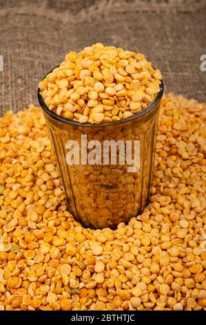 Petits pois jaunes dans un verre coupé et gris éparpillés sur un fond de toile de jute à texture grossière. Céréales traditionnelles pour faire des soupes et du porridge. CLO Banque D'Images