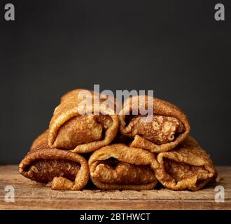 crêpes fines torsadées avec remplissage se trouvent dans une pile sur un panneau en bois, fond noir Banque D'Images