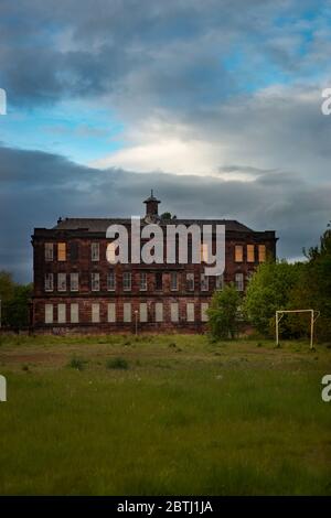 Un bâtiment scolaire délabré avec des fenêtres arraisonnées et des terrains surcultivés à Glasgow, en Écosse Banque D'Images