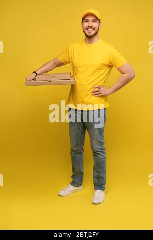 Portrait du jeune livreur en uniforme jaune avec des boîtes à pizza isolées sur fond jaune. Banque D'Images