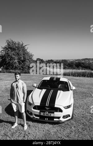 Un jeune homme musclé barbu pose avec sa voiture de sport Ford Mustang, prise en noir et blanc Banque D'Images