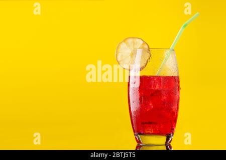 verre de boisson non alcoolisée avec beaucoup de glace une tranche de citron et une paille sur fond jaune Banque D'Images