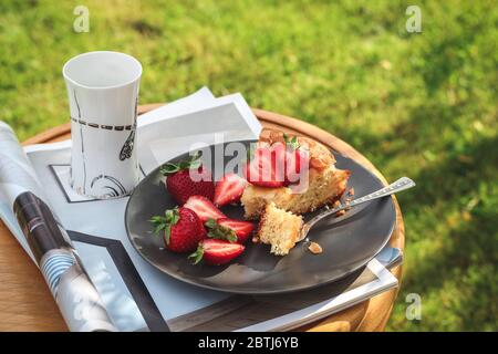 Une tranche de gâteau fait maison avec des fraises et une tasse de café sur un tabouret dans un jardin Banque D'Images