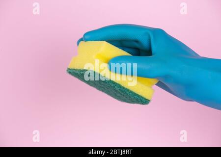Une main avec des gants de nettoyage tenant le tampon à récurer sur fond rose Banque D'Images