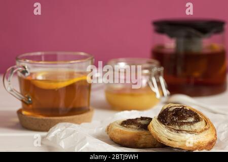 Petits pains à la cannelle faits maison, feuilleté et servi avec du thé noir, du citron et du miel dans un bocal pour le petit déjeuner. Banque D'Images