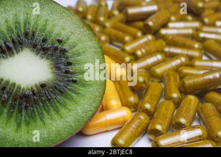 Complément de vitamines nutritionnelles concept: Macro gros plan de kiwis vert mûr frais et coupé en demi-tranches avec pile de capsules brunes et jaunes (foyer Banque D'Images