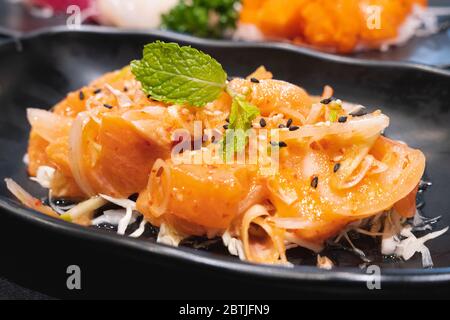 Salade de dés de saumon épicée de style thaïlandais nommée légume et herbe de yum. Servi sur une assiette noire en céramique blanche. Banque D'Images